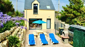 A house with a patio area featuring lounge chairs and a table, surrounded by a garden with purple flowers. - BEACH 30 m, 3 bedrooms, 2 WC, Garden,Private Parking,electricity, water included (Barneville-Carteret)