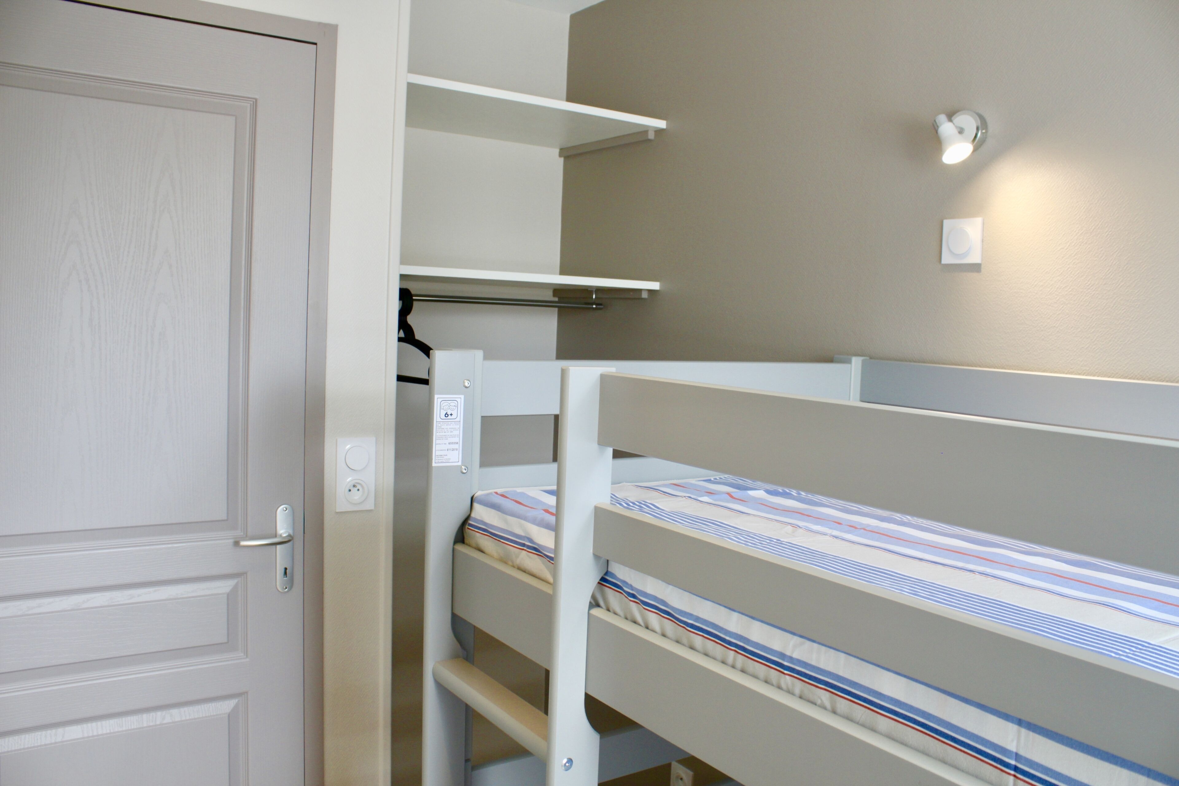 A bedroom with bunk beds, a door, and a light fixture on the wall.