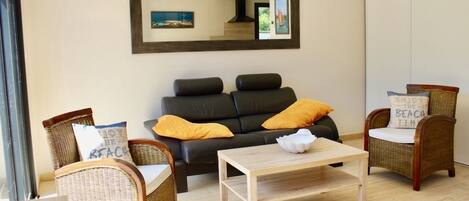 Una sala de estar con un sofá, dos sillones de mimbre, una mesa de centro y un espejo grande en la pared.