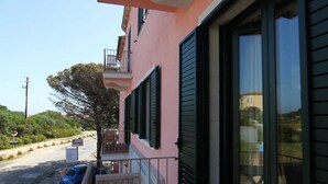 A pink building with a balcony, a parked car, and a tree in the background. - B&B treatment in La Maddalena, Sardinia (La Maddalena)