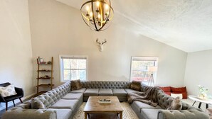 A spacious living room with a large sectional sofa, a wooden coffee table, and a decorative deer head mounted on the wall.