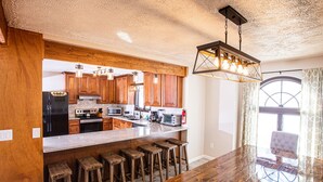 A spacious kitchen with wooden cabinets, a large island with stools, and modern appliances.