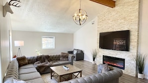 A living room with a sectional sofa, a fireplace, a mounted TV, and a chandelier.