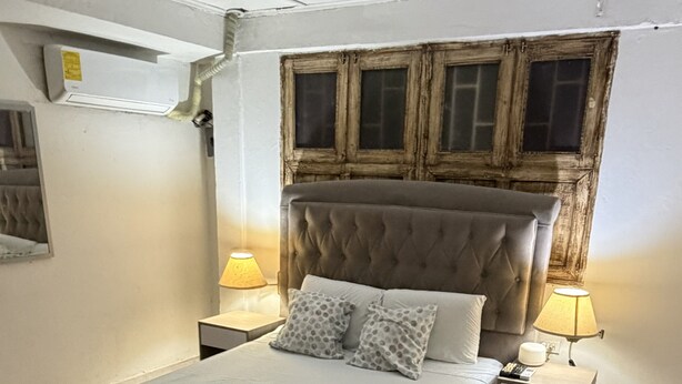 A bedroom with a bed, two bedside tables, a window with wooden frames, and an air conditioning unit. - 10 min walled city Single Aptment / Getsemani_301 (Cartagena)
