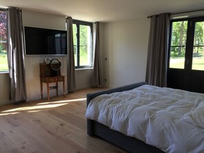 Une chambre avec un grand lit, un téléviseur fixé au mur et un bureau avec une lampe.