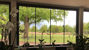 Une pièce dotée de grandes fenêtres donnant sur un terrain de golf, une table ornée de plantes en pot et une chaise.
