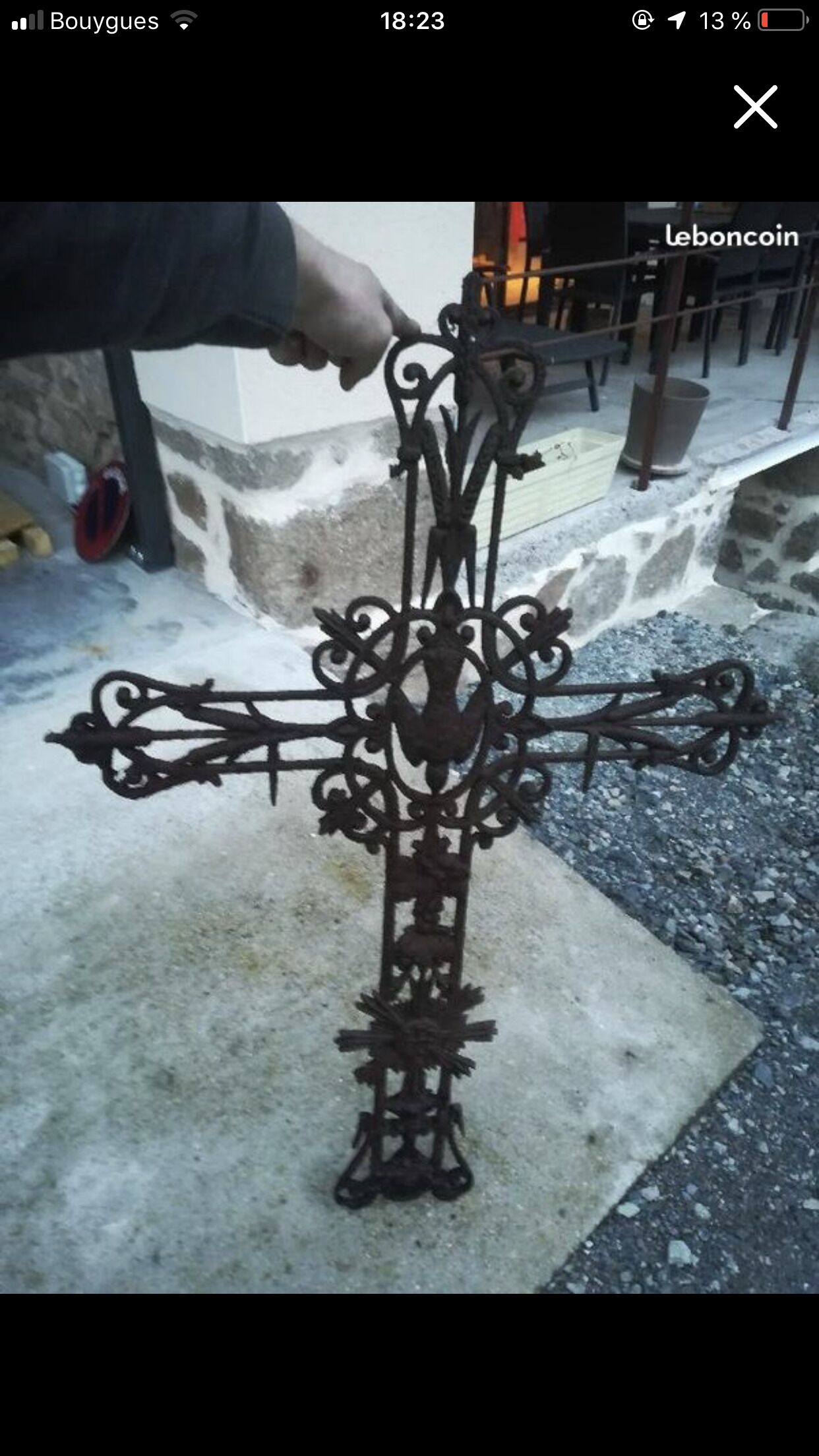A wrought iron cross with intricate designs, placed on a concrete surface outdoors.