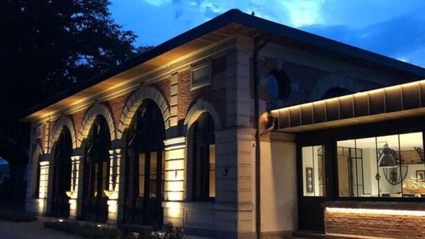 Un bâtiment à la façade en briques, doté de fenêtres en arc de cercle et d’une extension moderne avec de grandes fenêtres.