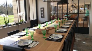 Une longue table à manger, dressée avec de la verrerie verte et des assiettes blanches, entourée de chaises.