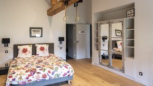 Une chambre à coucher avec une couvre-lit à motifs floraux, un plafond en bois, une armoire avec un miroir et une porte donnant sur une autre pièce.