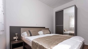 Quarto moderno com cama grande, mesa de cabeceira com abajur e guarda-roupa com espelho.