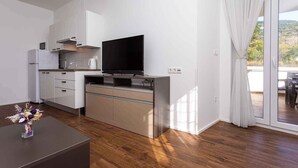 Uma cozinha moderna com armários brancos, uma TV de tela plana e uma área de jantar com mesa e cadeiras.