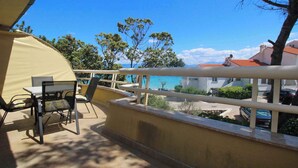 A balcony with a table and chairs, overlooking a coastal area with trees and buildings.