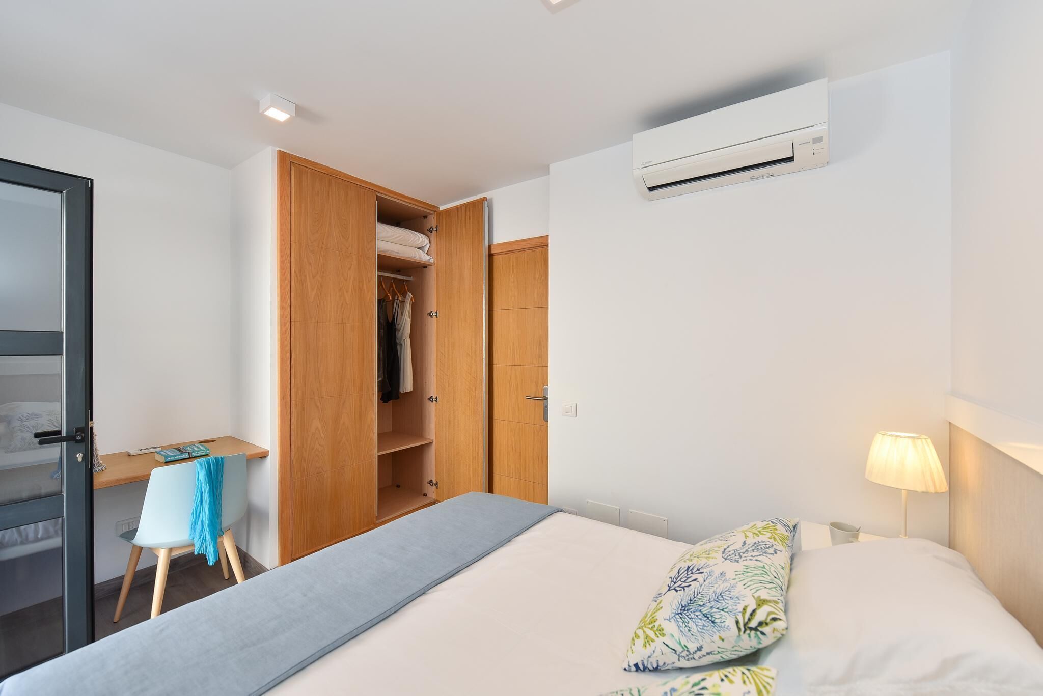 A bedroom with a bed, a desk, and an open wardrobe.