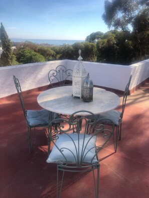 A round table with four chairs and two lanterns on a terrace with a view of the sea and trees. - Holiday Flat With Sea Views (Mojácar)