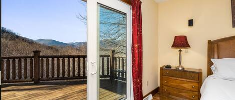 Una camera da letto con pavimento e comò in legno, un letto, un comodino, una lampada e un'ampia porta finestra che dà su una terrazza esterna con ringhiera.