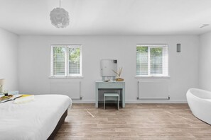 Une chambre moderne avec un lit, un bureau et deux fenêtres équipées de stores.
