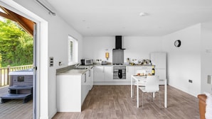 Una cucina moderna con mobili bianchi, piano cottura a gas, forno a microonde e lavello. C'è una zona pranzo con un tavolo e sedie bianche.