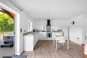 A modern kitchen with white cabinets, a gas stove, a microwave, and a sink. There is a dining area with a white table and chairs.