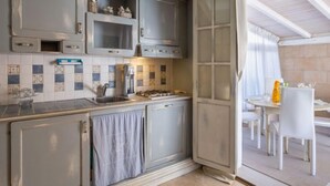 Een keuken met grijze kastjes, een betegelde spatwand, en een eethoek met witte stoelen en een tafel.