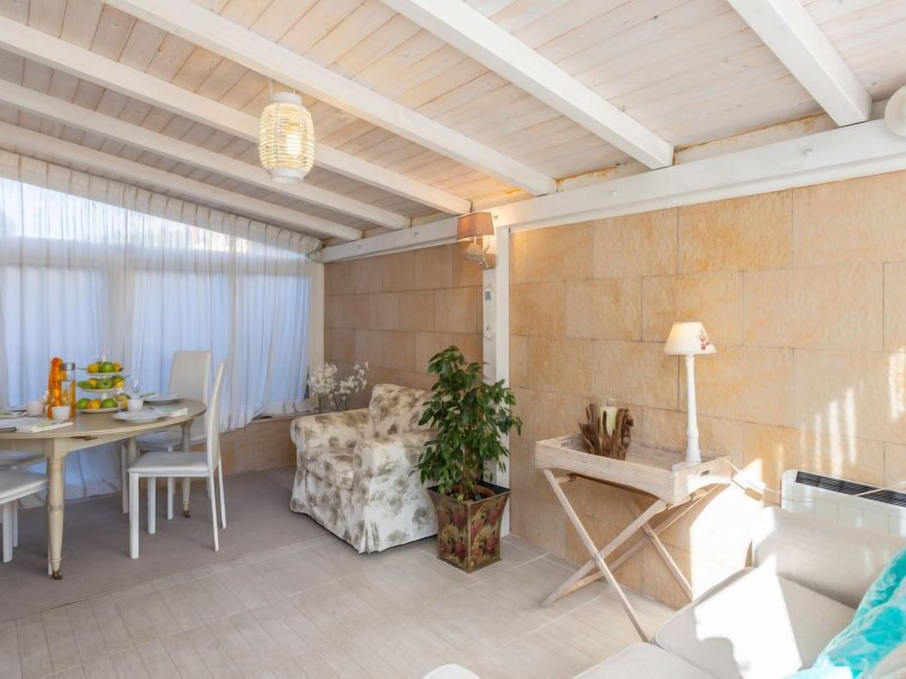 A modern living room with a dining area, featuring a wooden ceiling, a large potted plant, and a white sofa.