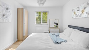Ein Schlafzimmer mit einem Bett, einem Nachttisch, einem Spiegel und einem Fenster mit Jalousien.