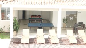 A covered outdoor area with a foosball table, lounge chairs, and a ping pong table.