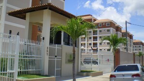 A multi-story residential building with a gated entrance, palm trees, and a parked car.