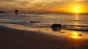 Una playa al atardecer con una torre de salvavidas, mar tranquilo y huellas en la arena.
