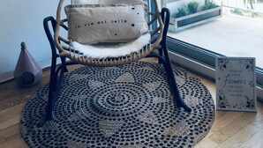 Una silla de mimbre con un cojín mullido y una alfombra de ganchillo sobre un suelo de madera.