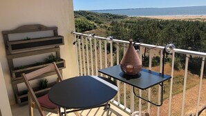 Un balcón con una mesa y sillas, con vista a una playa y zona boscosa.