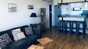 Una sala de estar moderna con un sofá negro, una mesa de centro de madera y una zona de cocina con un taburete de bar.