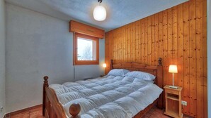 Ett sovrum med en sänggavel i trä, en enkelsäng, ett nattduksbord med en lampa, ett fönster och en taklampa.