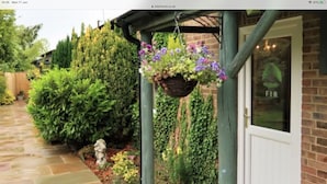 Uma trilha de pedra leva a uma casa com uma cesta de flores pendurada e uma porta com a placa 'FIR'.