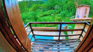 Una escalera de madera que lleva a un balcón con vistas a un paisaje verde exuberante, una piscina y un edificio pequeño.