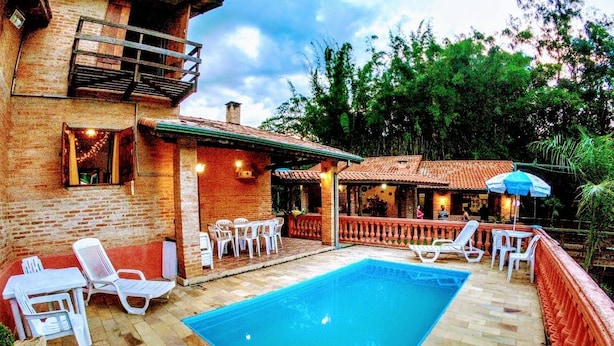 Una piscina rectangular con un deck de baldosas, rodeada de sillas y mesas de descanso blancas.