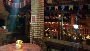 Comedor interior con paredes de ladrillo, faroles colgantes y una mesa con mantel a cuadros.
