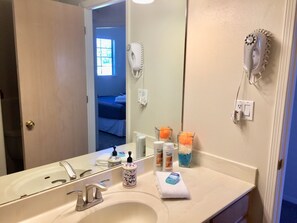 A bathroom with a sink, mirror, hair dryer, and toiletries.