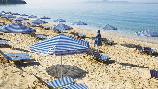 Ein Strand mit blauen, gestreiften Sonnenschirmen und Liegestühlen.