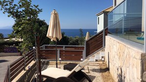 Eine Terrasse mit Liegestuhl und Sonnenschirm, mit Blick auf eine schöne Seelandschaft.