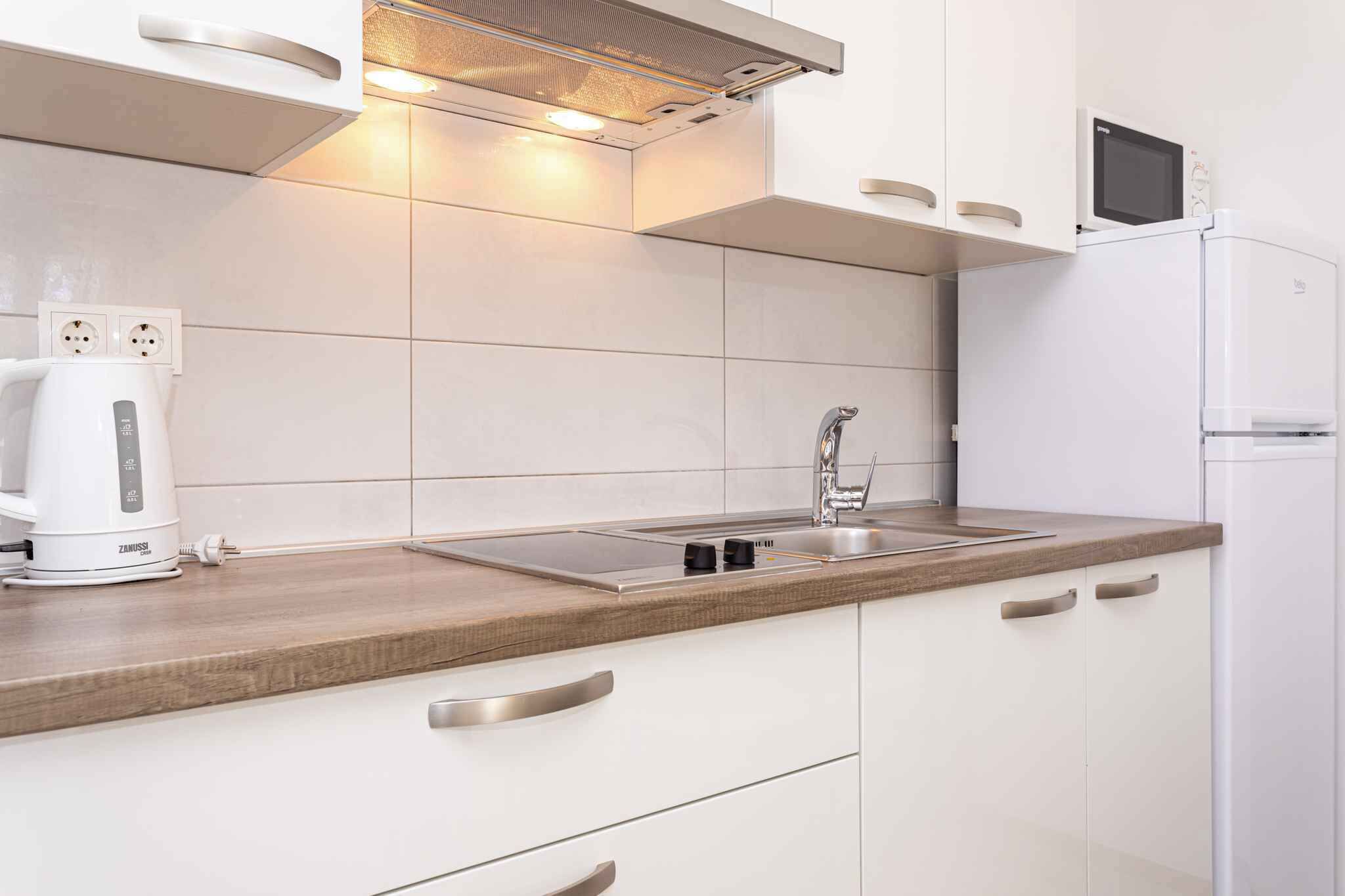 Una cocina moderna con armarios blancos, un lavamanos de acero inoxidable, un microondas integrado y una tetera sobre la encimera.