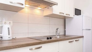 Una cocina moderna con armarios blancos, un lavamanos de acero inoxidable, un microondas integrado y una tetera sobre la encimera.