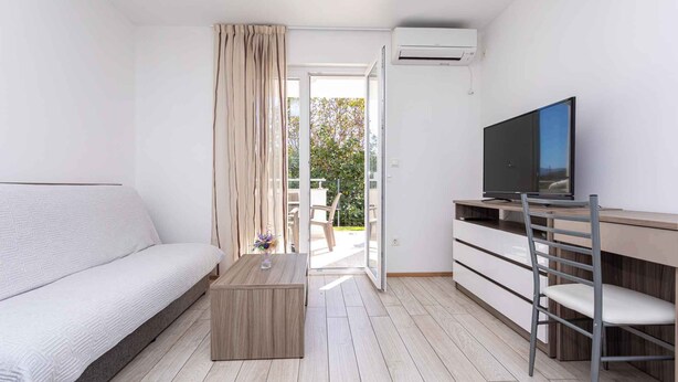 Una habitación moderna y bien iluminada con sofá, televisión, escritorio y una silla.