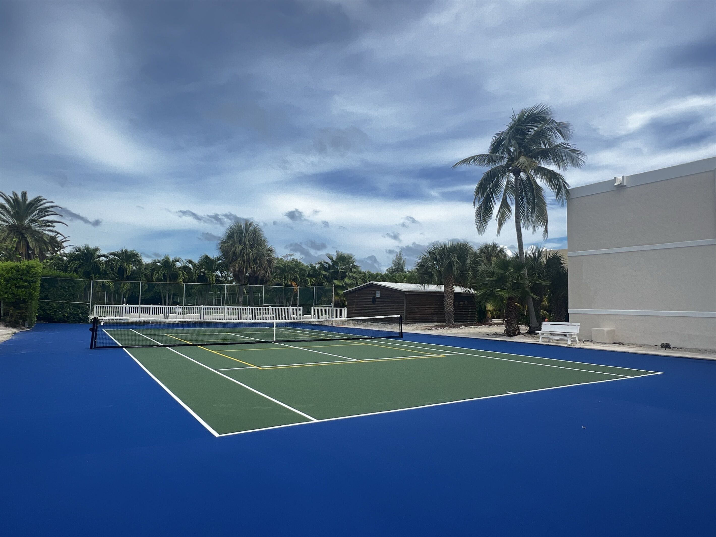 Un court de tennis avec un filet, entouré de palmiers et d’un bâtiment.