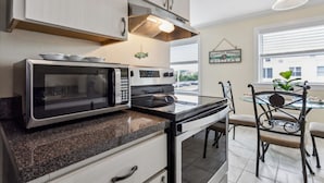 A kitchen with a microwave, stove, and dining area with chairs and a table. - 1 block to beach & boardwalk | Central Downtown (Virginia Beach)