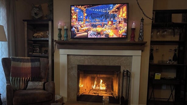 A cozy living room with a fireplace, a television displaying a festive scene, and a comfortable armchair.