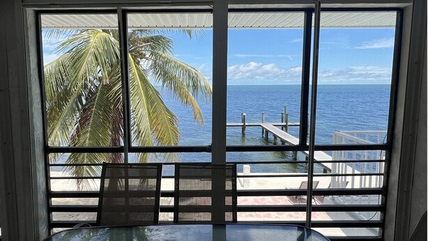 Ein Zimmer mit großem Fenster mit Blick auf einen Strand und den Ozean, ausgestattet mit einem Tisch und Stühlen.