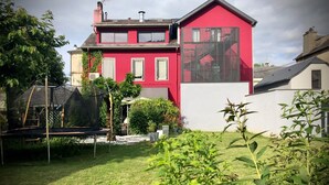Een rode, twee verdiepingen tellende woning met een groot raam en een witte muur.
