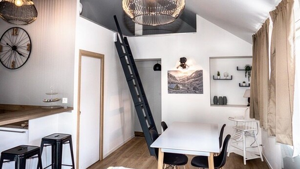 Een moderne keuken met een wit aanrecht, zwarte krukken en een hanglamp.