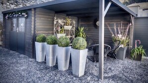 Een overdekt terras met een muur van natuursteen, plantenpotten en een metalen poort.